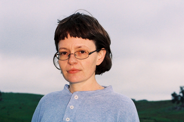 Portrait of singer-songwriter Ruby Gill wearing glasses and a light blue shirt outdoors.